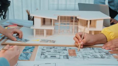 A group of architects and designers actively collaborating around a table filled with blueprints and models, showcasing creativity and teamwork in planning projects. SACTR