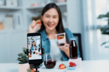 Seçici odaklı akıllı telefon ve gülümseyen genç, güzel Asyalı karışık çilek ve kiraz suyu detoksu değerlendirmesi sosyal medyada sağlıklı ürün tanıtımı sunuyor. Taktik.