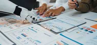 Üretken bir ortamda robot kolun yanında çalışan, veri analizi ve yenilikçi teknolojinin ön plana çıkarıldığı bir ofis sahnesi. Noogenesis