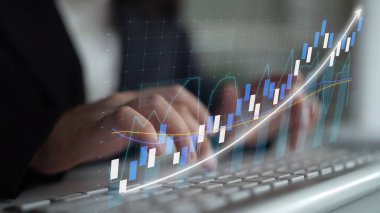 A business professional focuses on financial data analysis, using digital graphs and charts that represent market trends and growth in a modern corporate setting. Copula