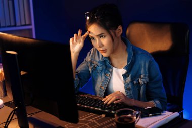 Stresli, genç, güzel Asyalı yaratıcı proje yaratıcısı sosyal medyayı araştırmak için bilgisayara bakıyor ve geceleri daha çok neon modern ofisin planlama kanalı stratejisine ulaşılıyor. Taktik.