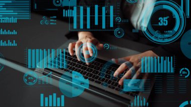 A business professional types on a laptop surrounded by digital graphics representing data analysis, illustrating contemporary technology in a professional workspace. Xenic